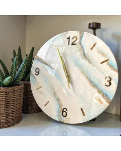 ساعة حائط مصنوعة يدويًا من الريزن الإيبوكسي بألوان عاجية وزرقاء ومرصّعة بالكريستال لإطلالة أنيقة وراقية.